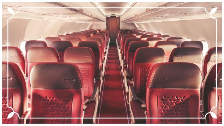 A wide-angle interior view of an airplane cabin with window shades open during takeoff.